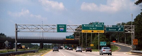 Highway exit sign on Interstate 295 South in New Jersey, showing directions to Delran and Rancocas Woods, with cars traveling under a clear sky.